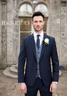 a man wearing a suit and tie standing in front of a stone building with the words benefitti written on it