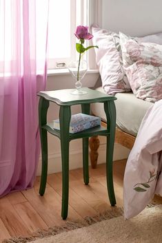 a small green table with a flower in a vase on it next to a bed