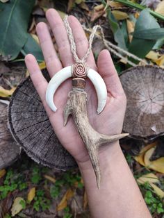 a hand holding an animal horn with two horns on it's end and a spiral bead necklace hanging from the middle