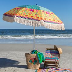 an umbrella and chair on the beach with towels under it, next to the ocean