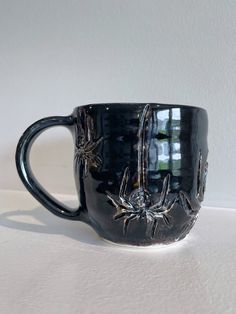 a black coffee cup with spider webs on the outside and inside, sitting on a white surface