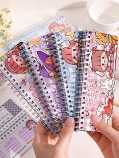 four notebooks with stickers on them are being held by someone's hands