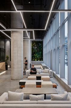 a person sitting on a couch in a large room with lots of windows and concrete columns