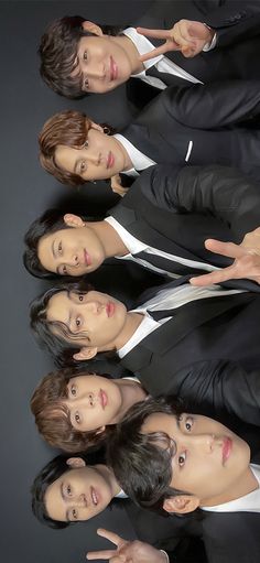 four young men in suits posing for a photo together, with one pointing at the camera