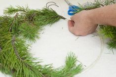 someone using scissors to trim a pine wreath