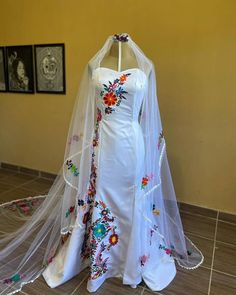 a white wedding dress with colorful flowers on it and a veil hanging from the back