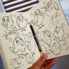 a hand holding an open coloring book with cartoon characters on it and a pencil in the middle