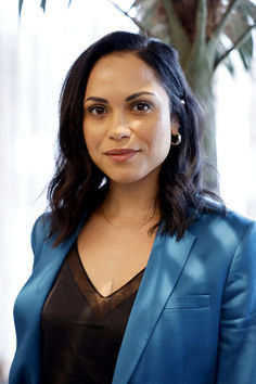 a woman standing in front of a potted plant wearing a blue blazer and black top