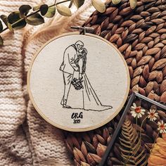 a hand embroidered picture of a bride and groom holding each other in front of a basket with flowers