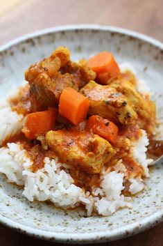 a white plate topped with rice and meat covered in gravy on top of a wooden table