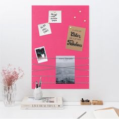 a pink bulletin board with pictures and notes attached to it, sitting on a desk