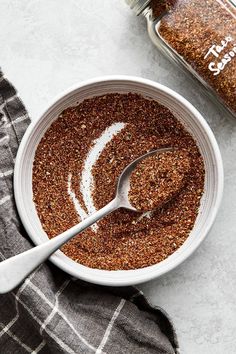 a white bowl filled with spices next to a jar of seasoning on top of a towel