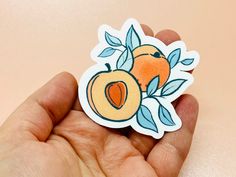 a hand holding a sticker with an orange and leaves design on the back of it