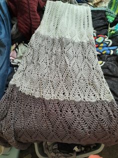 a knitted blanket sitting on top of a pile of clothes