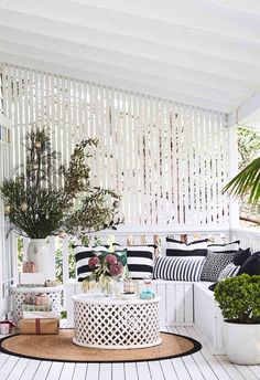 a white porch with black and white striped pillows on the floor, potted plants in vases