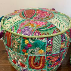 a colorful patchwork ottoman with tassels on the top and bottom, sitting on a wooden floor