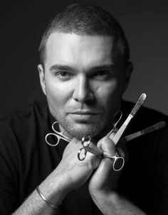 a black and white photo of a man with scissors in his hands, looking at the camera