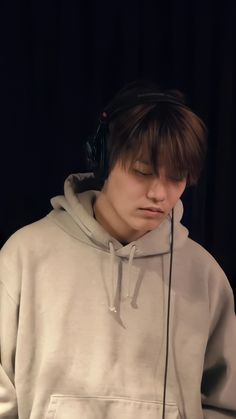 a young man wearing headphones while standing in front of a black background with his eyes closed