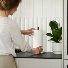 a woman is holding a roll of toilet paper in front of a potted plant