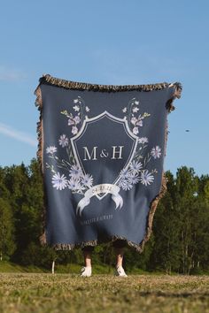 a person standing in the grass holding up a blue blanket with white flowers on it