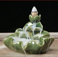 a green and white ceramic fountain with water pouring out of it's sides on a wooden table