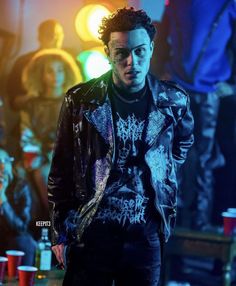 a young man in a leather jacket standing next to a table with cups on it