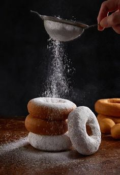 a person sprinkling sugar on some doughnuts