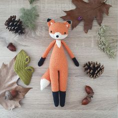 an orange stuffed animal laying on top of a wooden table next to leaves and acorns