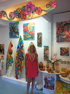 a woman standing next to surfboards in a room with paintings on the walls and ceiling