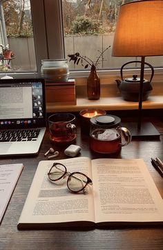 an open book sitting on top of a desk next to a laptop computer and glasses