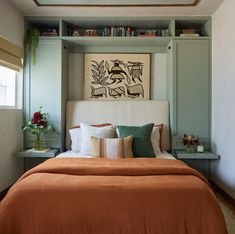 a bed with an orange comforter and pillows in a room that has bookshelves on the wall