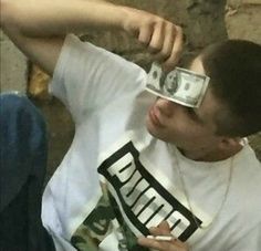 a man with money covering his eyes while sitting on the ground in front of a stone wall