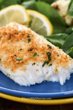 a piece of fish on a blue plate with spinach leaves and lemon wedges