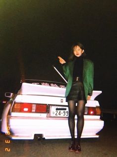 a woman standing next to a white car with her hand on the back of it