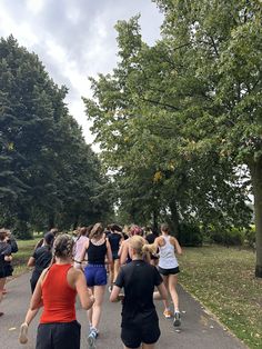 a group of people running down a road next to trees and grass on a cloudy day