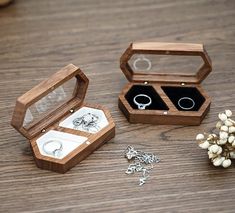 an open wooden box with two rings and some other jewelry on the table next to it