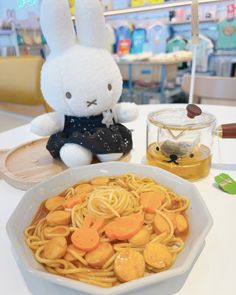 a bowl of noodles with carrots, and a stuffed rabbit sitting on the table