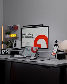 a desk with a computer, phone and other items on it in front of a gray wall