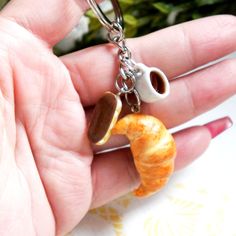 a hand holding a tiny keychain with a coffee cup and saucer on it