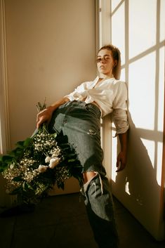 a woman leaning against a wall with flowers in her lap and holding onto the door