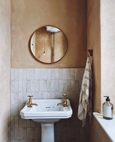 a white sink sitting under a round mirror in a bathroom next to a bathtub