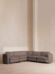 a large gray sectional sofa sitting on top of a wooden floor next to a white wall