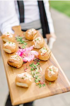 a person holding a wooden tray filled with small pastries on top of a table