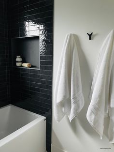 two white towels are hanging on the wall next to a bathtub and shelf in a black tiled bathroom