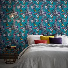 a bed with white linens and pillows in front of a blue floral wallpaper