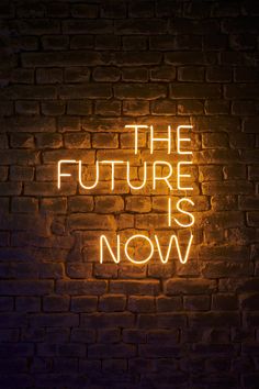 the future is now neon sign on a brick wall in front of a dark background