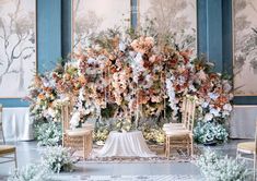 an elaborate floral arrangement is displayed in front of two gold chairs and a white table cloth