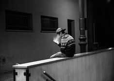 a person sitting on a ledge talking on a cell phone while wearing a baseball cap