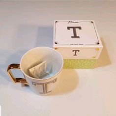 a coffee cup with the letter t on it next to a boxed teabag and box