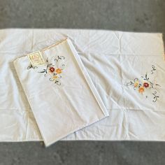 two white linens with embroidered flowers on them sitting on the floor next to each other